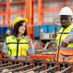 female supervisor advises technician foreman to inspect spare part equipment of production machine conveyor belt, team of diverse workers working together at industrial manufacturing factory