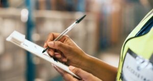writing and hands with clipboard in warehouse, supply chain and quality assurance report. Factory, notes and person with checklist for stock distribution, shipping or inspection for export