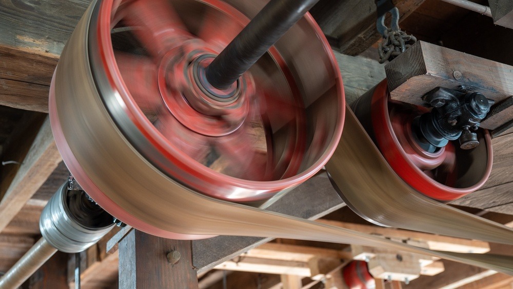 ​Functioning antique belt-drive system inside a water-powered grain mill. The photo shows the transfer of power through a series of pulleys and leather flat belts, illustrating 19th-century industrial engineering.